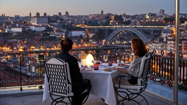 A couple dining at a table with a city view, featuring a bridge and buildings.