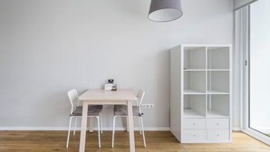 A room with a white table and chairs, a white shelving unit, and a hanging light fixture.