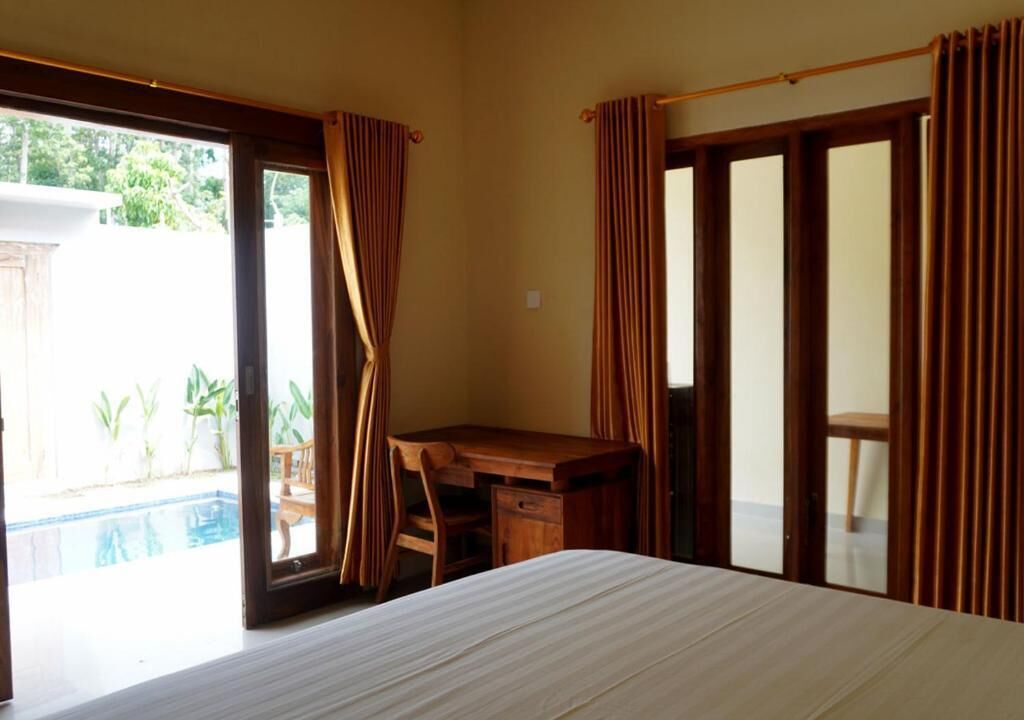 A bedroom with a bed, a desk, and a view of a swimming pool.
