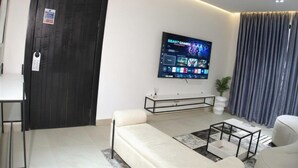 Een moderne woonkamer met een bank, salontafel, een aan de muur bevestigde televisie en een deur met slot.