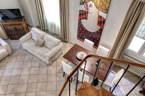Ein Wohnzimmer mit einer Couch, einem Esstisch mit Stühlen, einem Fernseher auf einem Schrank und einer Heizung.
