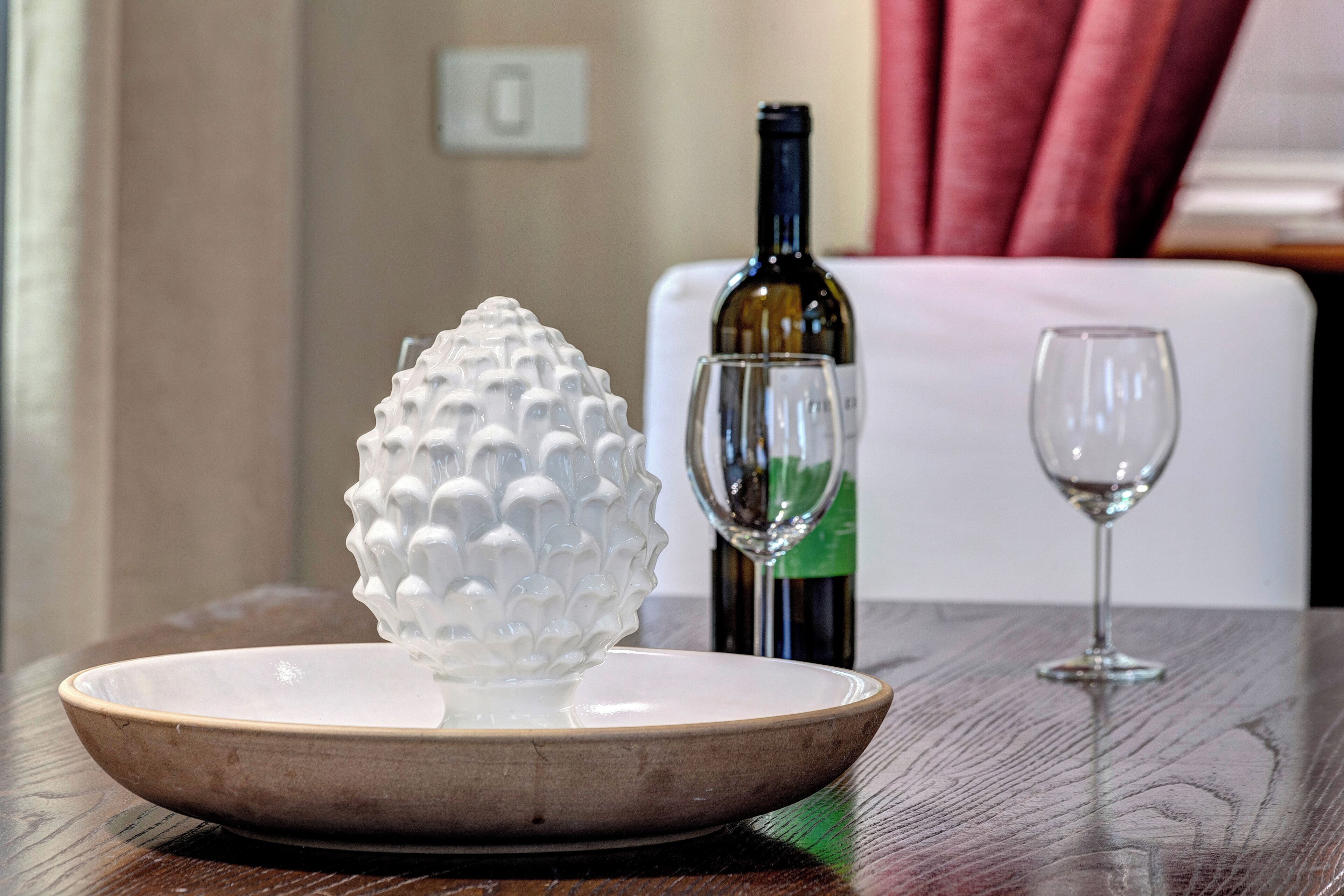 Un bol blanc à texture sur une assiette, une bouteille de vin et deux verres à vin sur une table en bois.