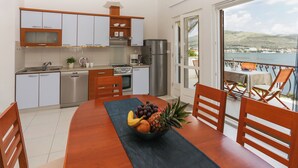 A modern kitchen with stainless steel appliances, a dining area with a wooden table and chairs, and a balcony with a view of the sea. - Villa Anita – for 10 Guests with Private Pool, Okrug Donji (Okrug Donji)