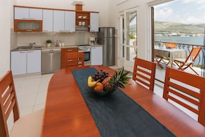 A modern kitchen with stainless steel appliances, a dining area with a wooden table and chairs, and a balcony with a view of the sea. - Villa Anita – for 10 Guests with Private Pool, Okrug Donji (Okrug Donji)