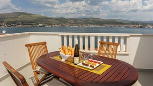 A wooden table with a bottle of wine, bread, and tomatoes on a balcony overlooking a coastal town. - Villa Anita – for 10 Guests with Private Pool, Okrug Donji (Okrug Donji)