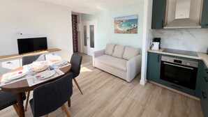 Eine moderne Küche mit Backofen von Bosch, ein Essbereich mit Tisch für zwei Personen, eine Couch und ein Fernseher.
