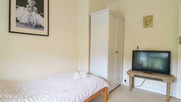A bedroom with a bed, a wardrobe, a television on a wooden stand, and a framed picture on the wall.