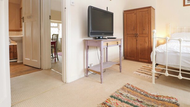 Ein Schlafzimmer mit Bett, einem Fernseher auf einem kleinen Tisch, einem Holzschrank und einer Tür zu einem Badezimmer.