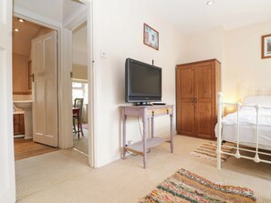 A bedroom with a bed, a television on a small table, a wooden wardrobe, and a door leading to a bathroom.
