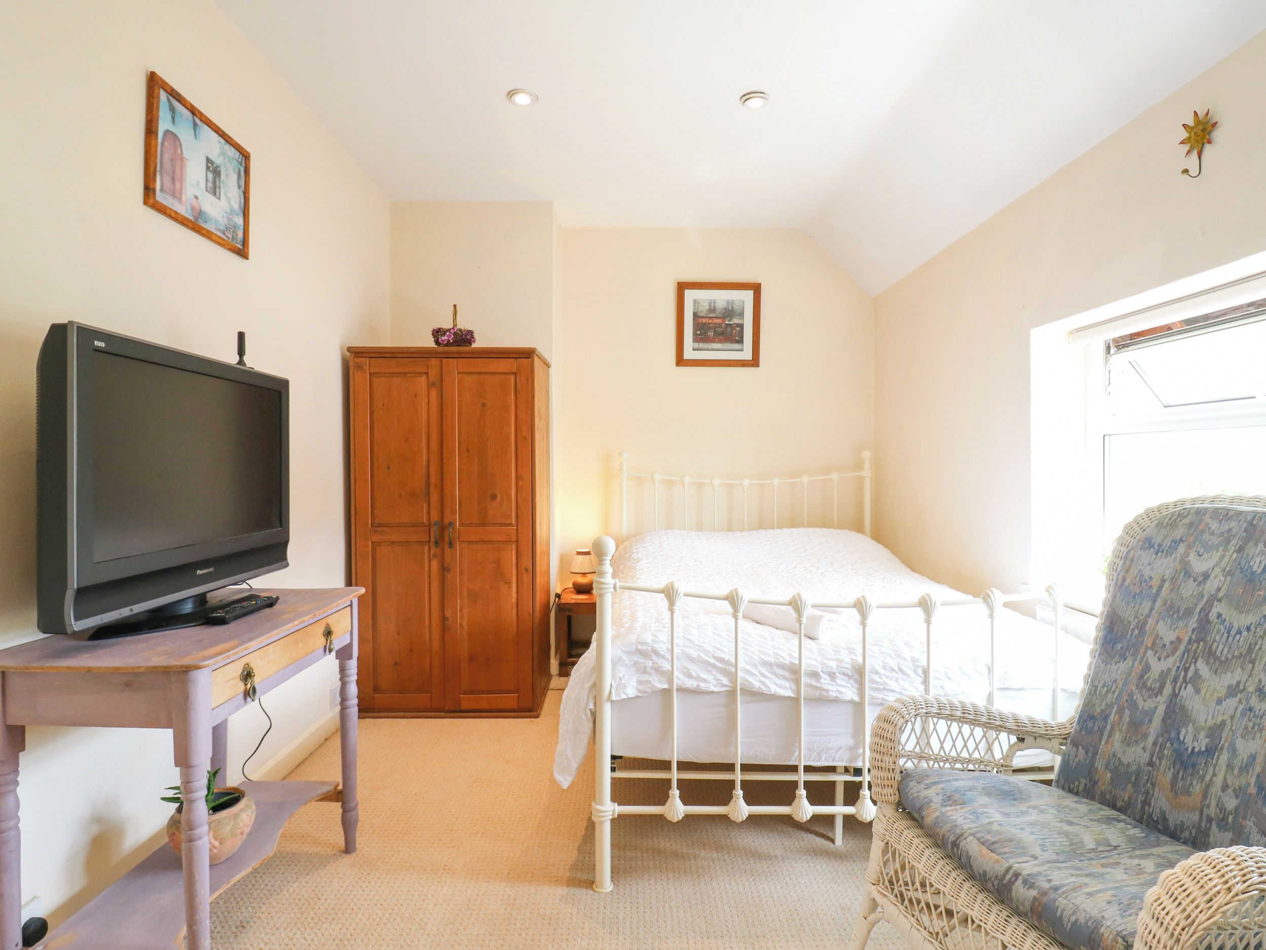A bedroom with a bed, a television on a table, a wardrobe, and a wicker chair.
