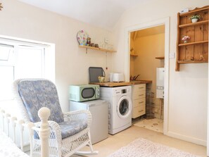 A compact living space with a washing machine, a microwave, a wicker chair, and a small kitchenette.