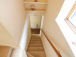 A carpeted staircase with a wooden handrail, leading to a landing with a radiator and a potted plant. - Daisy Cottage (Dorking)