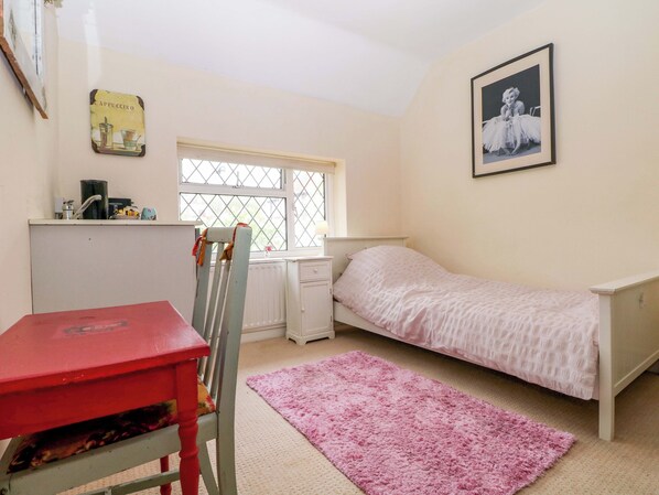 A bedroom with a bed, a desk, a chair, a window, and a framed picture on the wall.