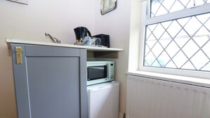 Eine kleine Küchenzeile mit Mikrowelle, kleinem Kühlschrank, Spüle und einem Fenster mit einem runden Lamellenrollo.