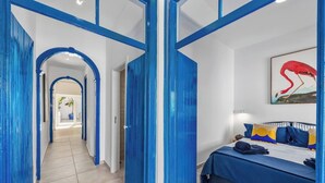 A hotel room with a bed, a painting, and a hallway with blue doors. - Charming 3BR historic townhouse in Portimão's old town, steps from the marina and promenade. Easy access to Algarve beaches. Sleeps 9. Self check-in via lockbox. (Portimão)