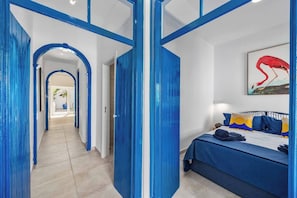 Une chambre d’hôtel avec un lit, un tableau et un couloir avec des portes bleues.