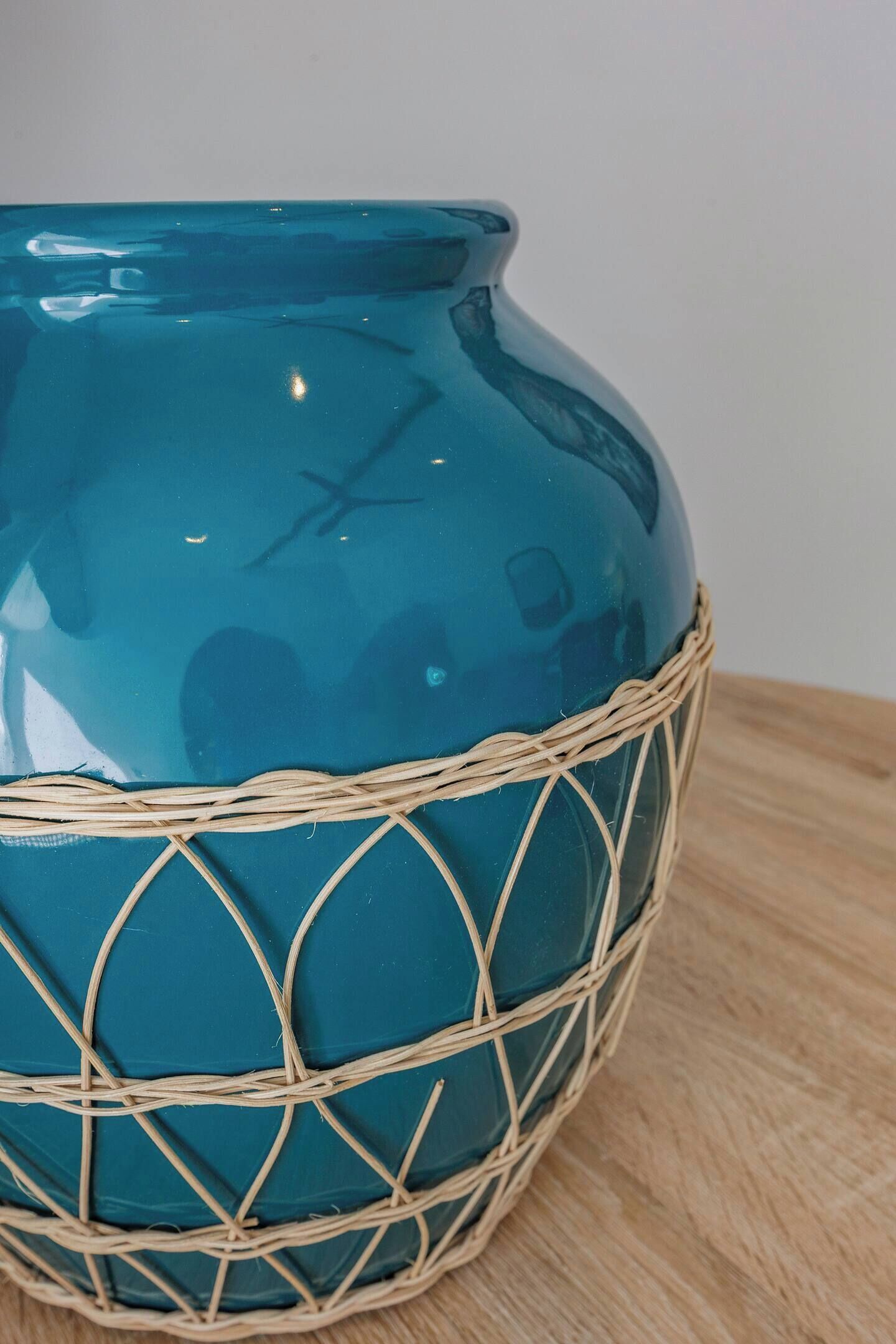 A teal vase with a woven basket base on a wooden surface.