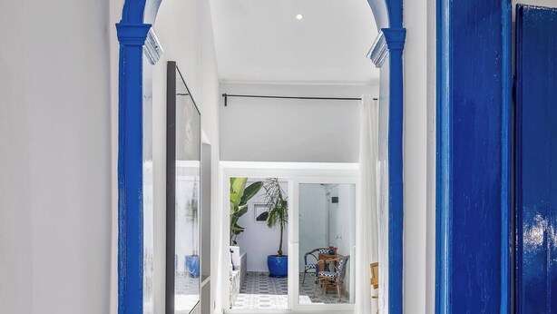 A hallway with a blue archway leading to a room with a large window, a potted plant, and a chair. - Charming 3BR historic townhouse in Portimão's old town, steps from the marina and promenade. Easy access to Algarve beaches. Sleeps 9. Self check-in via lockbox. (Portimão)