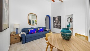 A modern living room with a blue sofa, wooden side table, and a round wooden dining table. - Charming 3BR historic townhouse in Portimão's old town, steps from the marina and promenade. Easy access to Algarve beaches. Sleeps 9. Self check-in via lockbox. (Portimão)