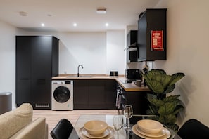 A modern kitchen with a washing machine, a dining area with a table set for two, and a plant. - City Point Aberdeen by Guestz (Aberdeen)