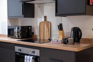 A modern kitchen with a microwave, toaster, kettle, and wooden cutting board. - City Point Aberdeen by Guestz (Aberdeen)