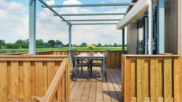 Eine Holzterrasse mit Tisch und Stühlen, einer Pergola und Blick auf ein grünes Feld.