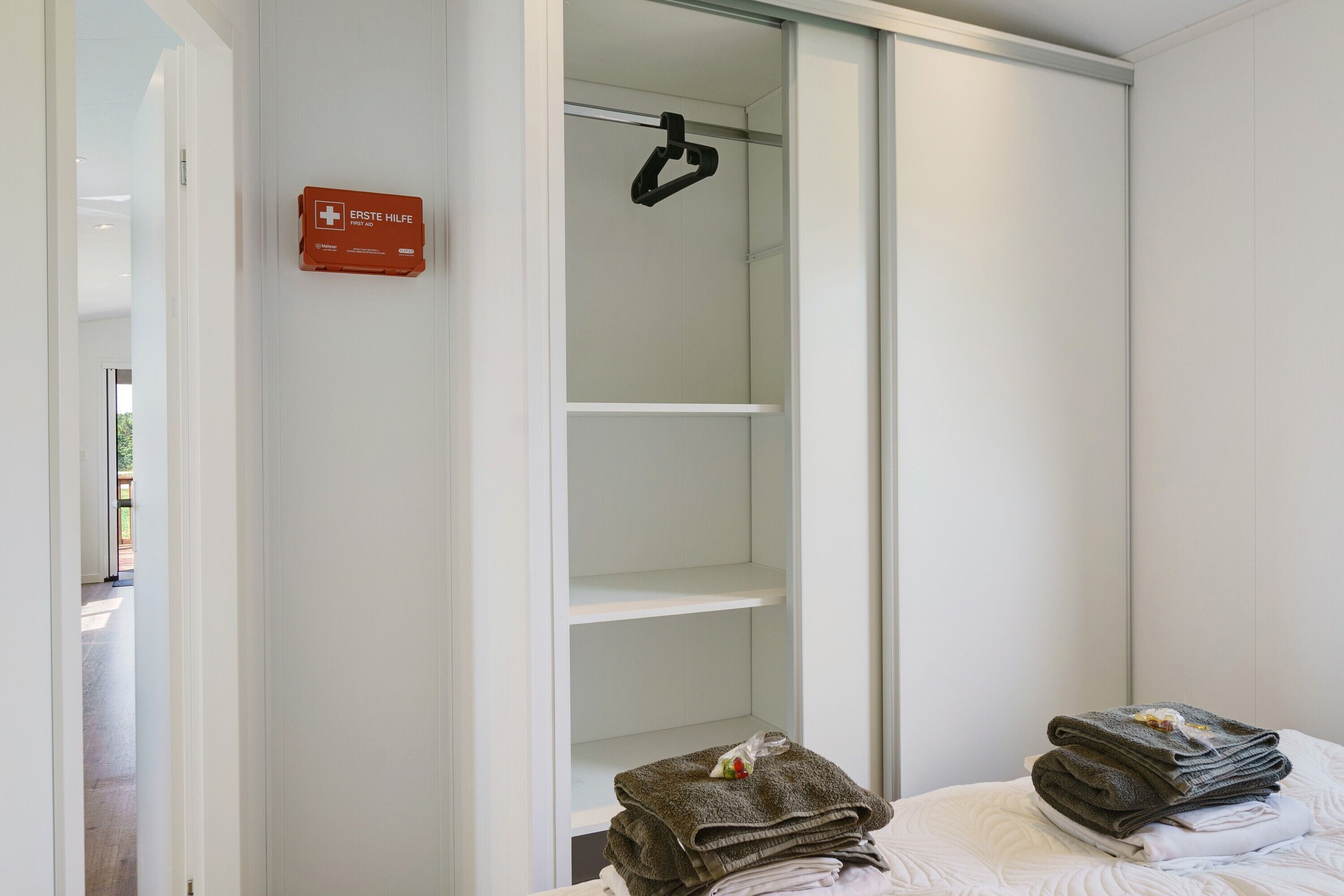 A room with a white wardrobe, a sign indicating first aid, and a bed with folded towels.