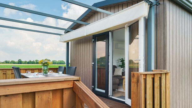 A wooden deck with a table and chairs, a sliding glass door leading to an indoor area with a sofa and a plant.