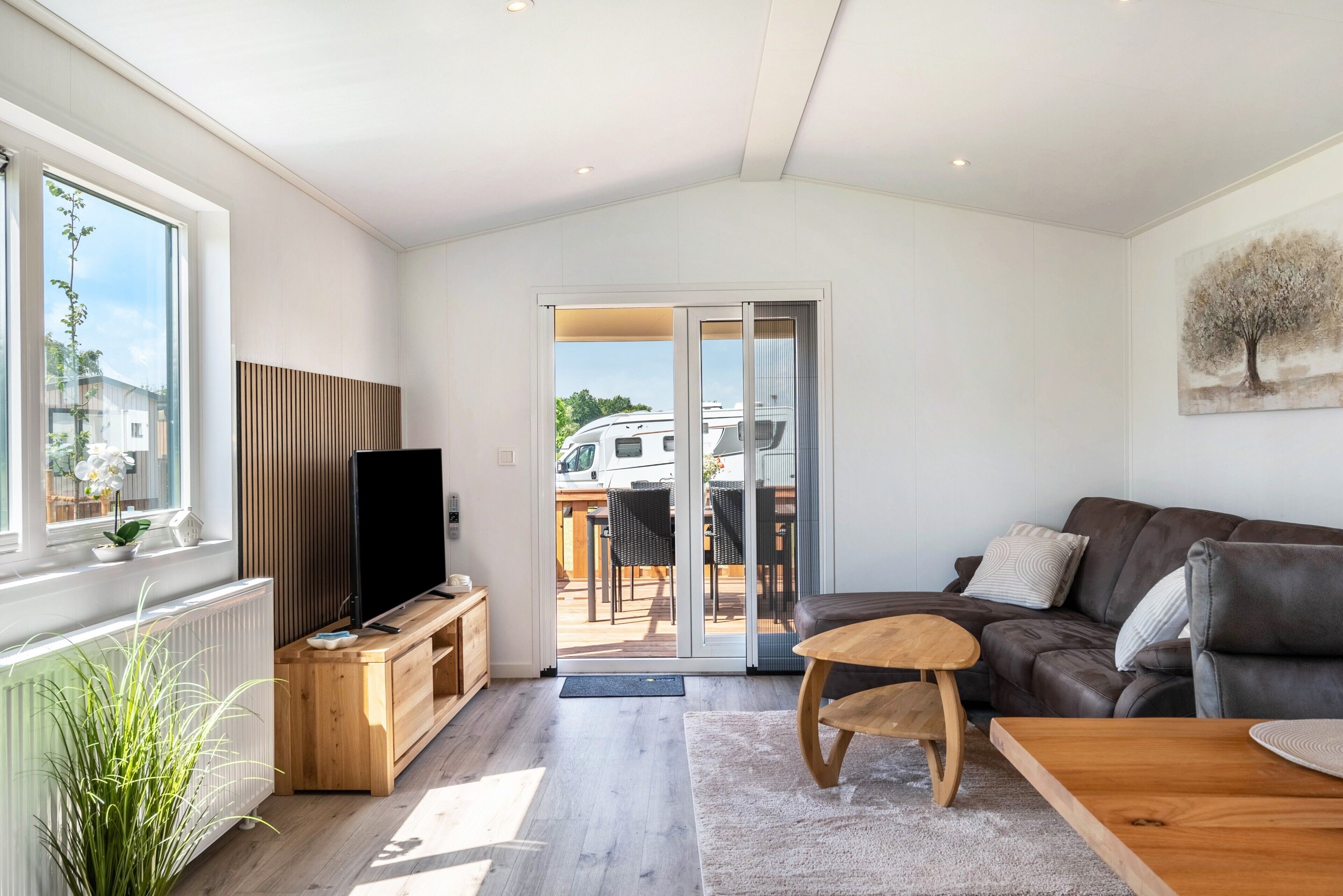 A modern living room with a flat-screen TV, wooden furniture, a sofa, and a sliding glass door leading to an outdoor area.