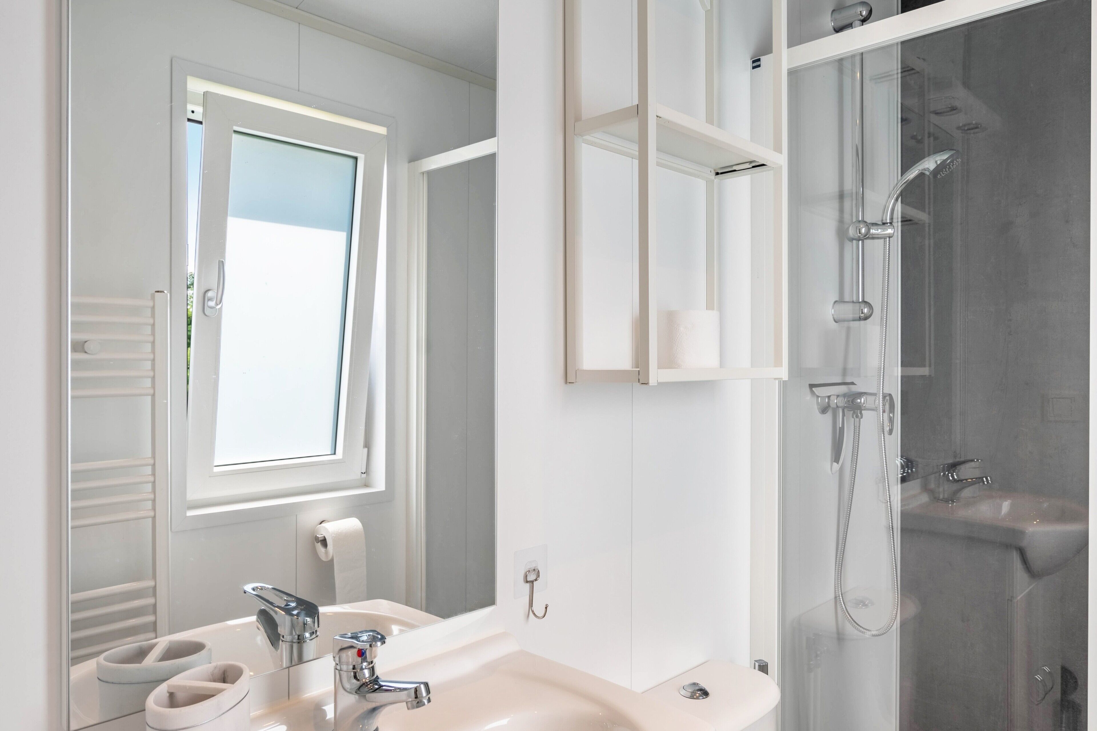Ein Badezimmer mit Waschbecken, Spiegel, Handtuchhalter und Dusche.