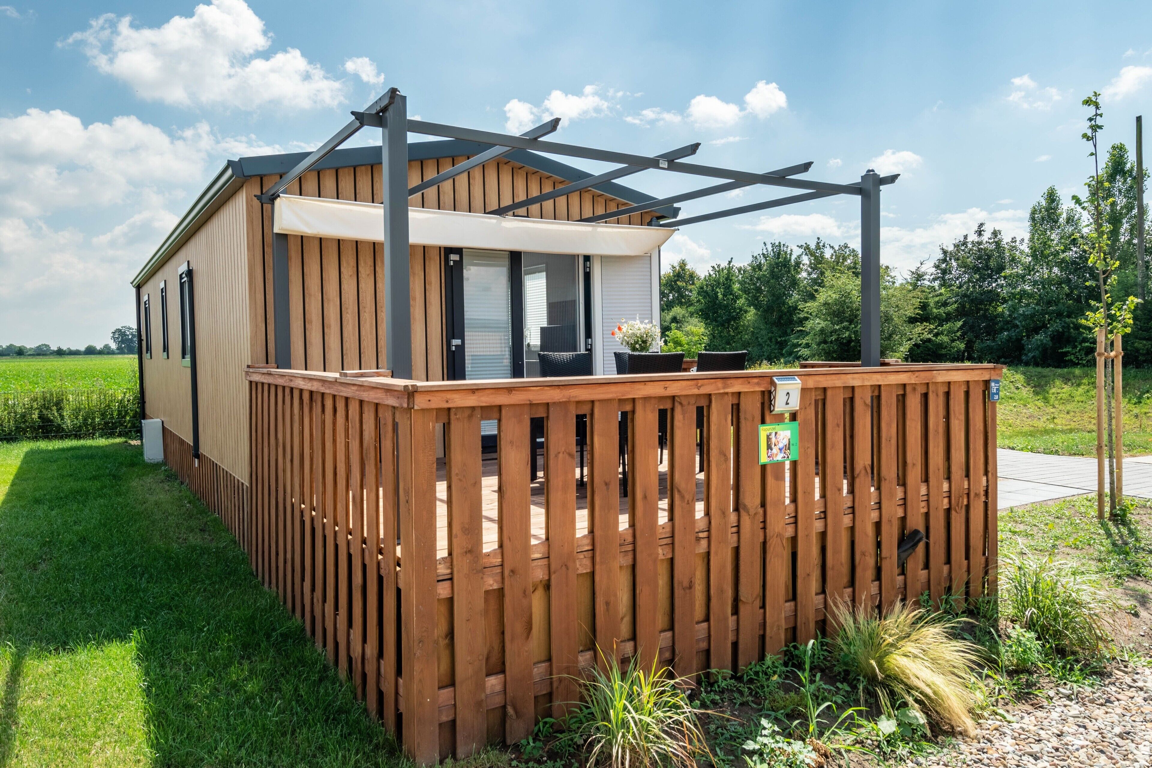 A wooden deck with a pergola, a small building with a sliding door, and a sign indicating room number 2.