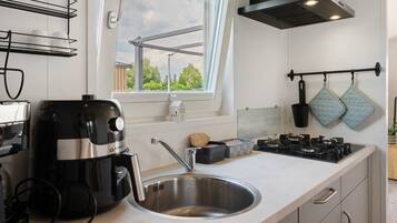 Eine moderne Küche mit Spüle aus Edelstahl, einer Kaffeemaschine, einem Herd und einem Fenster mit Blick auf Grünflächen.