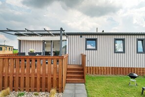 A modern house with a wooden deck, a barbecue grill, and a clear sky.