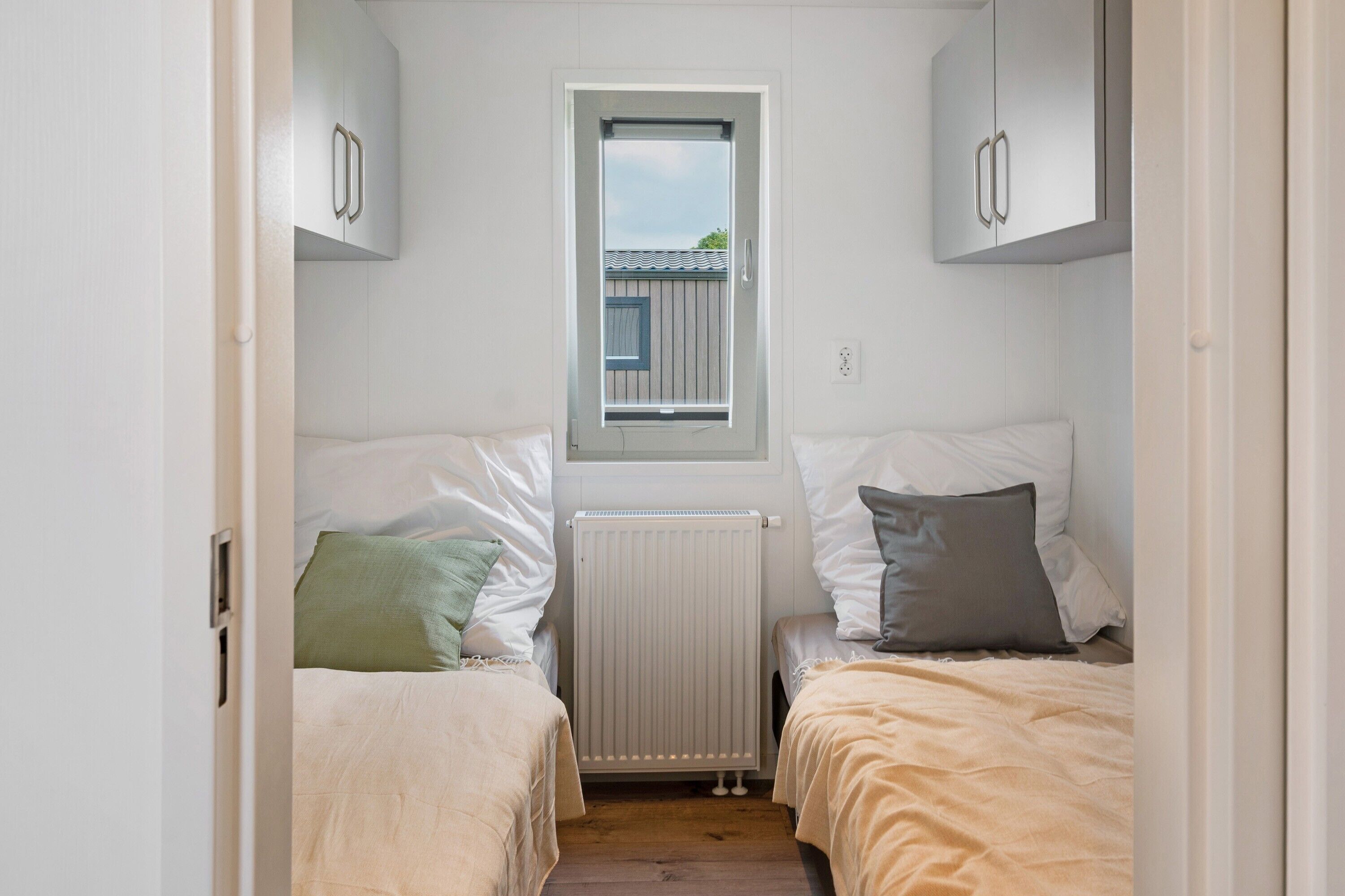 Habitación pequeña con dos camas, una ventana y un radiador.