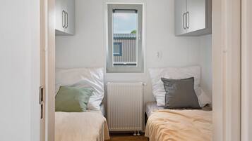 Habitación pequeña con dos camas, una ventana y un radiador.