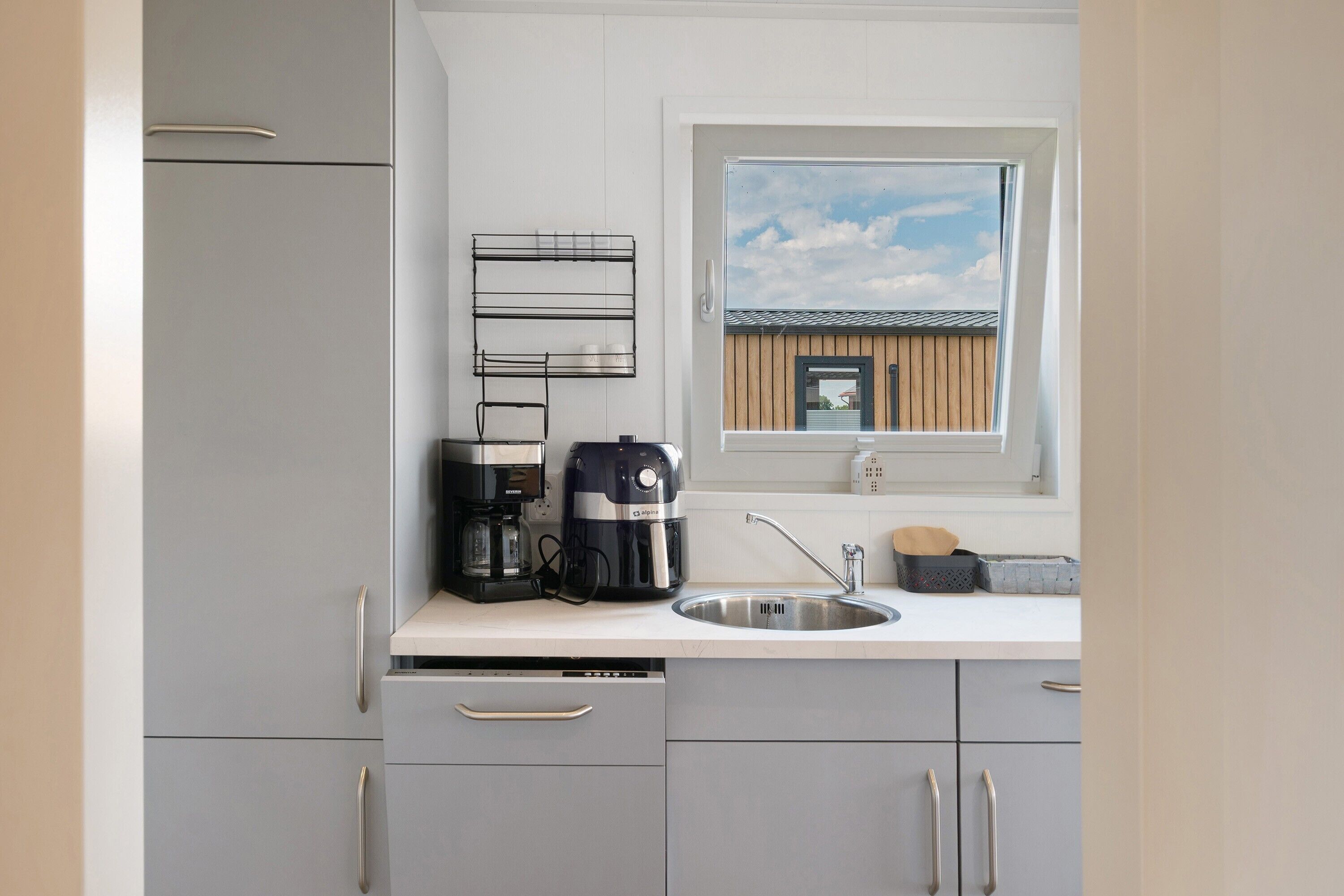 A modern kitchen with a built-in dishwasher, a coffee maker, and a window with a view of a building.