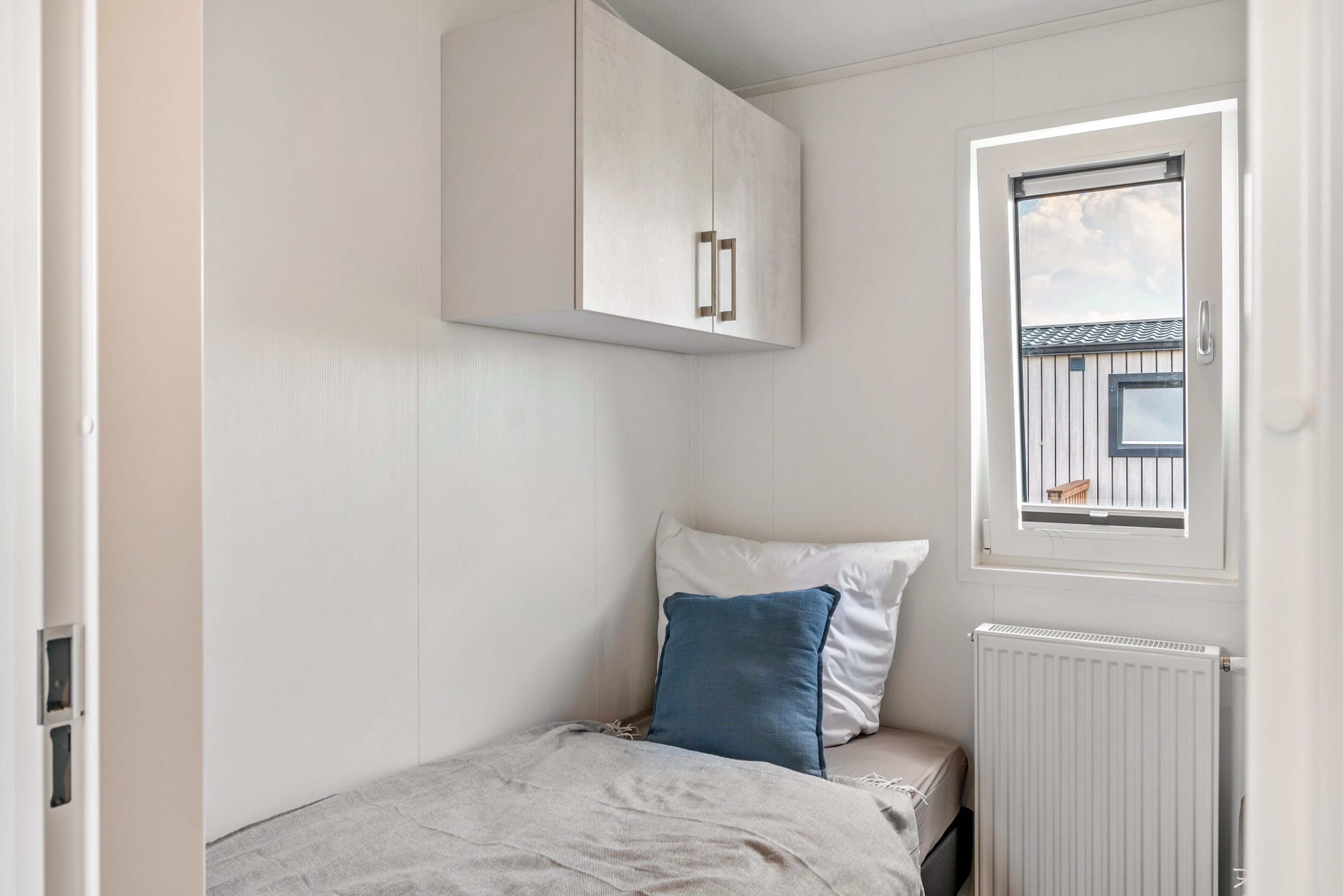 Une petite chambre avec un lit simple, une fenêtre donnant sur un paysage agréable, un radiateur et une armoire.