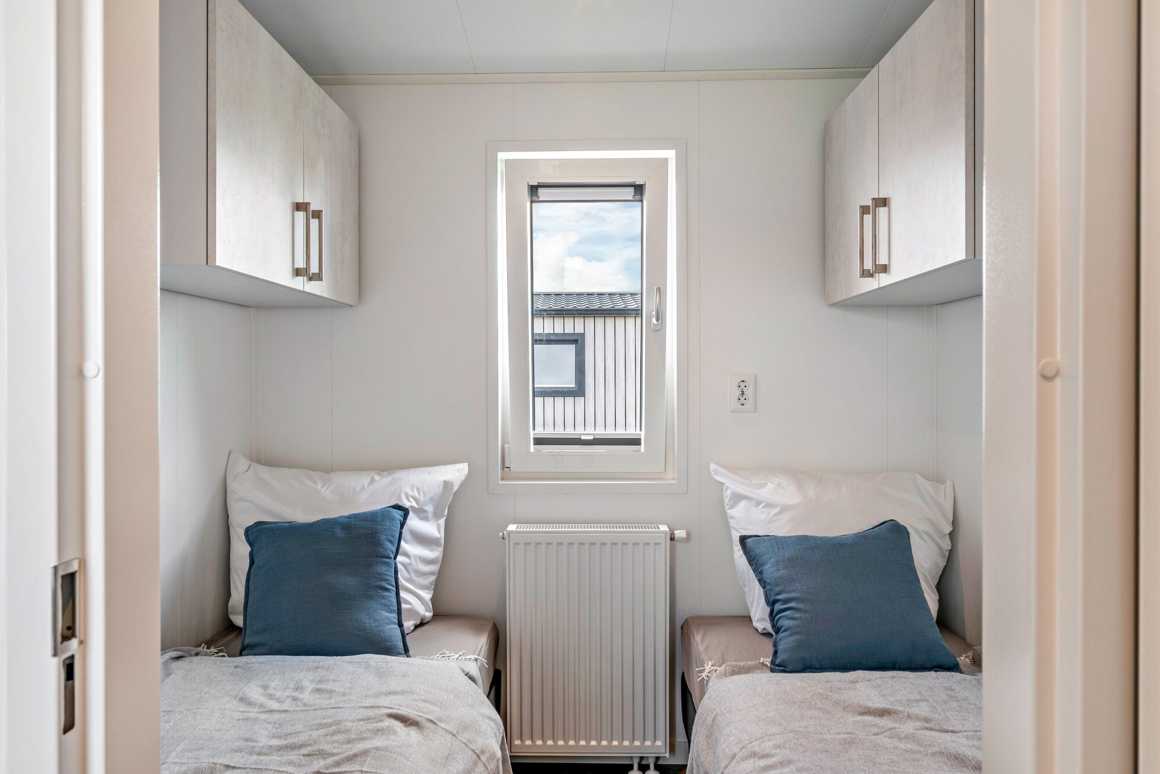 Ein kleines Zimmer mit zwei Betten, einem Fenster und einer Heizung.