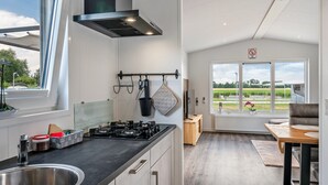 A modern kitchen with a gas stove, a built-in oven, and a large window overlooking a garden.