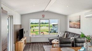 A modern living room with a large window, a sofa, a TV, and a dining area.
