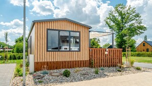 A modern wooden cabin with large windows, a gravel garden, and a wooden fence.