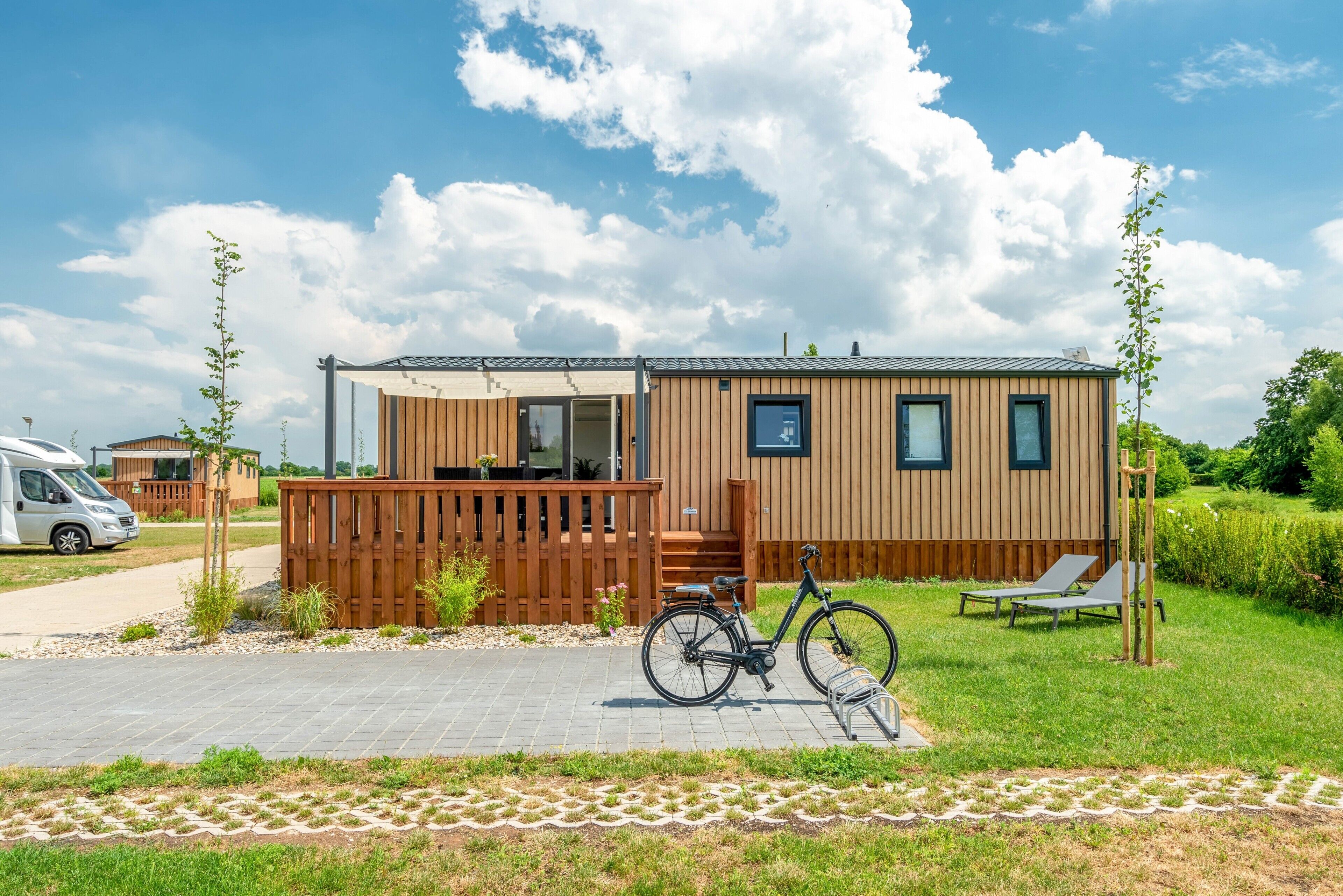 Une maison mobile avec une façade en bois, un vélo et une chaise de jardin.