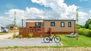 Une maison mobile avec une façade en bois, un vélo et une chaise de jardin.