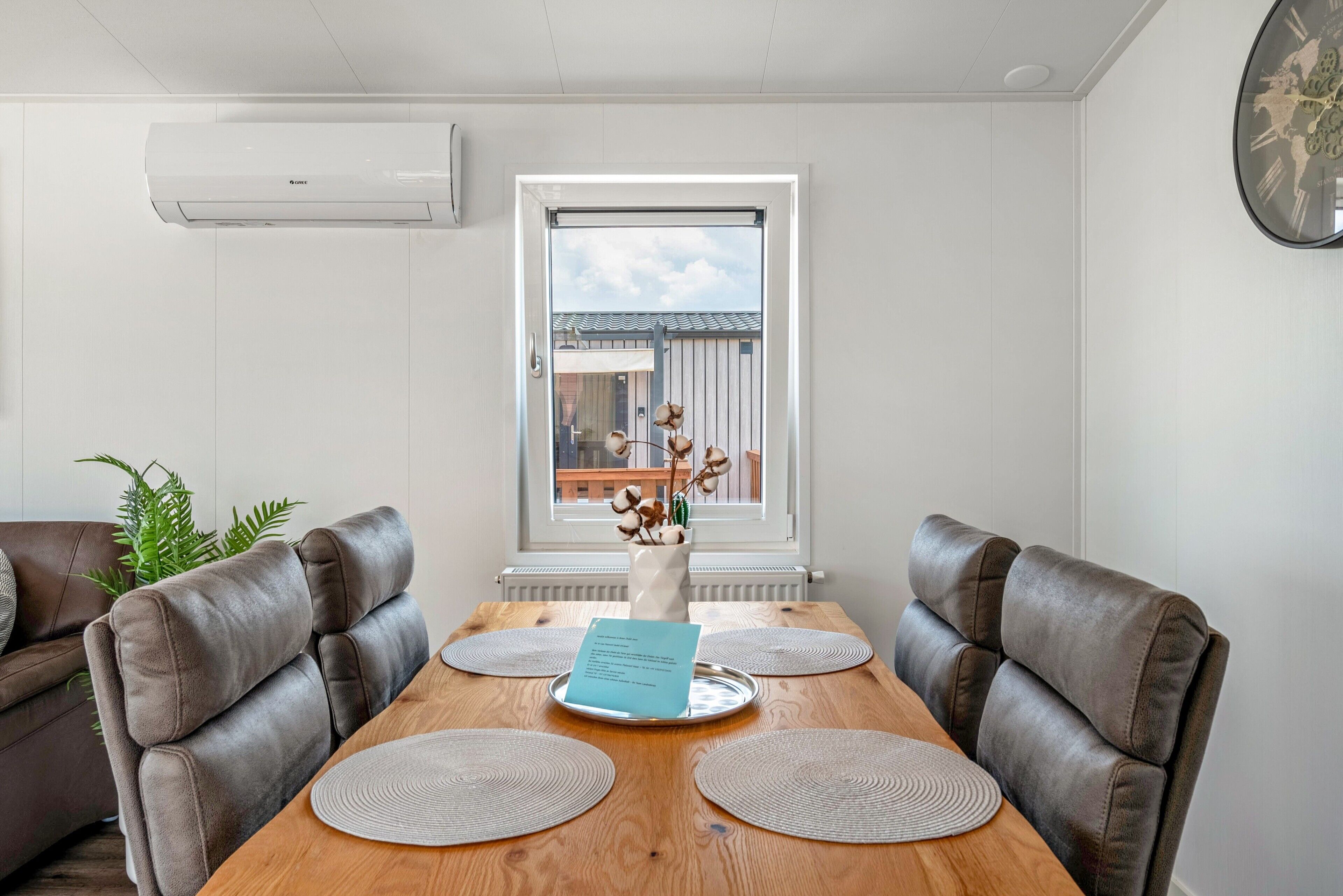 A dining area with a wooden table, leather chairs, a vase with flowers, and a view through a window.