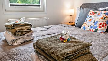 A neatly made bed with folded towels, a lamp, and a window with a view of greenery.
