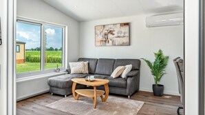 A modern living room with a grey sofa, a wooden coffee table, a large window with a view of greenery, and a painting on the wall.