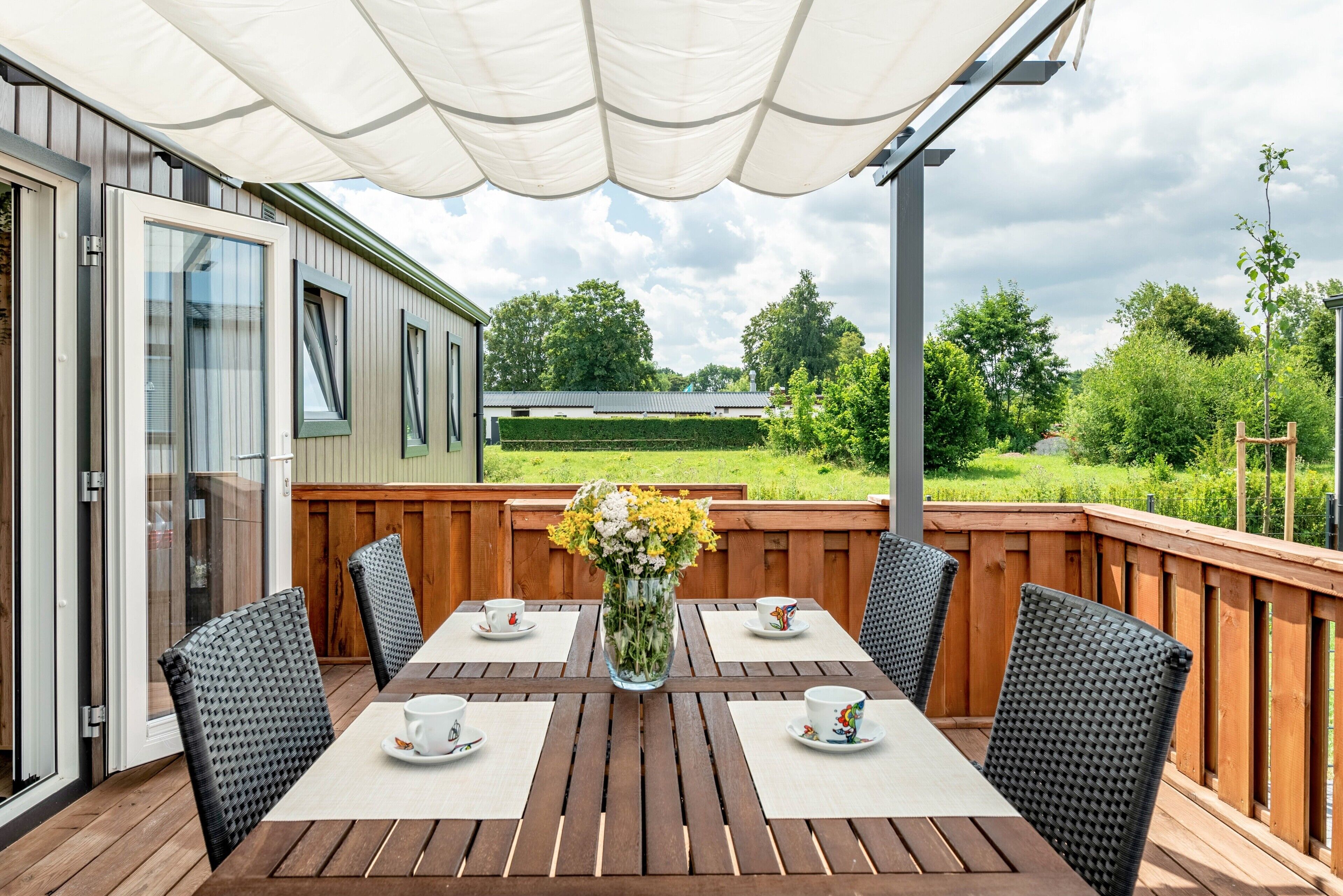 A deck with a wooden table and chairs, a white canopy, and a view of a green landscape.