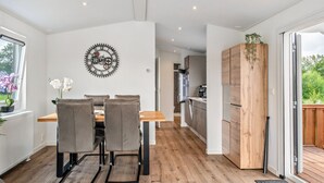 A modern kitchen with wooden cabinets, a dining area with a table and chairs, and a large window.