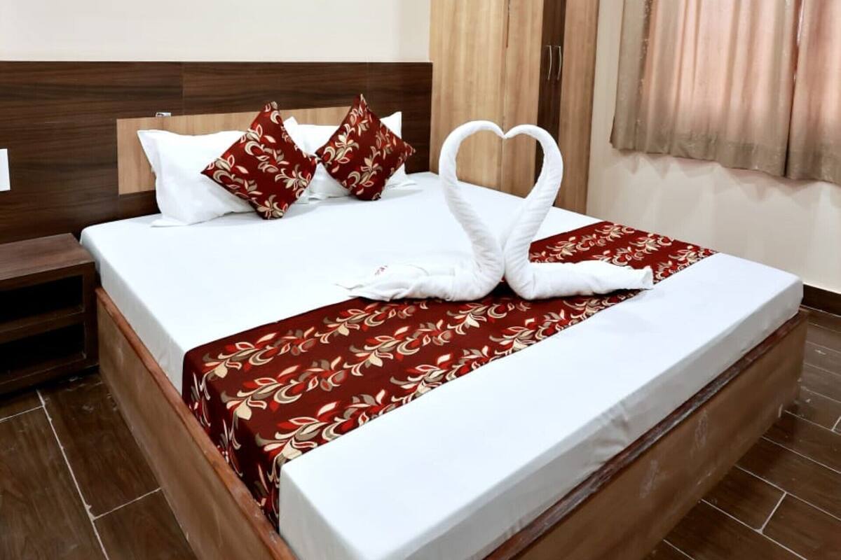 Una cama bien hecha con una toalla dispuesta en forma de corazón, un cabecero de madera, un ventilador de techo y un armario con cortina.