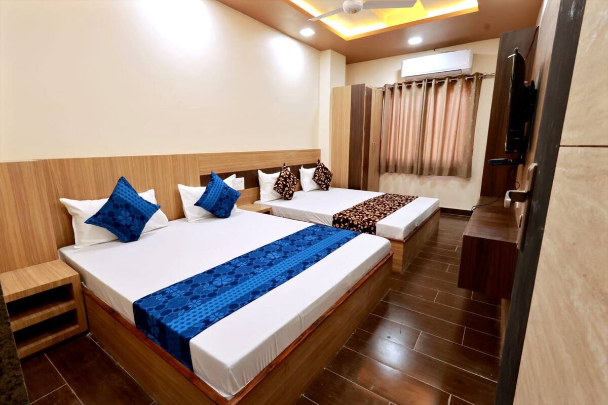 Habitación de hotel con dos camas, cabecera de madera, ventilador de techo, equipo de aire acondicionado y un pequeño escritorio.